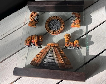May include: A decorative glass panel featuring Mayan-inspired relief sculptures. The panel includes a pyramid, a bear, and various figures in shades of orange, brown, and gray. The frame is made of dark wood.