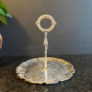 May include: Silver serving tray with a decorative handle and a scalloped edge. The tray has an ornate design.