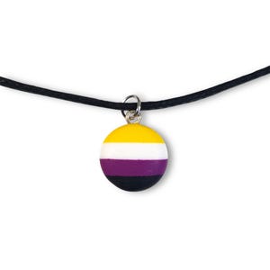 May include: A round pendant necklace with the non-binary pride flag colours: yellow, white, purple, and black. The pendant hangs from a black cord. The pendant is a circle with a silver-coloured bail.