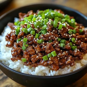 Puede incluir: Un bol de arroz blanco cubierto con carne picada, semillas de sésamo y cebolla verde picada.