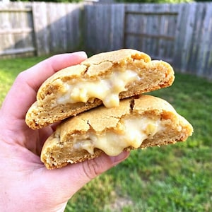May include: Two halves of a golden-brown cookie, revealing a creamy, white filling. The cookie's texture is slightly cracked, with the filling oozing out. The image is a close-up, highlighting the dessert's details.