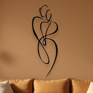 May include: A black metal wall art piece showing two figures embracing. The abstract design is mounted on a tan wall above a mustard-coloured sectional sofa. The room is decorated with neutral tones and natural light.
