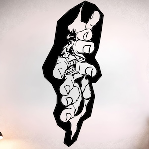 May include: A black and white wall decal depicting a stylized hand reaching out. The design includes a detailed illustration of a face with sharp teeth. The decal is applied to a white wall above a bed with colourful pillows.