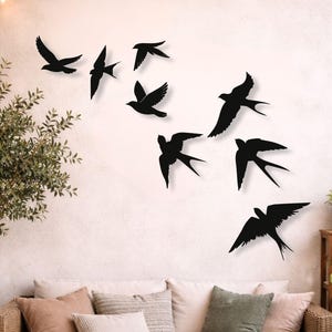May include: A set of seven black swallow bird wall decals arranged in a flying formation on a plain wall. Each bird silhouette features distinct wing shapes and forked tails, creating a dynamic visual effect of a flock in motion across the surface.
