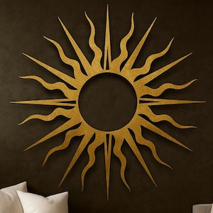 May include: A large, golden sunburst wall art piece with a circular center and radiating spiky and wavy rays. The sun is mounted on a dark wall above a gray sofa with white pillows and a brown throw blanket. A potted plant is to the left.