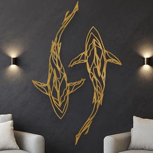 May include: Two gold-colored, stylized fish wall art pieces are mounted on a dark gray wall. The fish are facing each other, with intricate line details. The wall is flanked by two gray armchairs and sconce lighting.