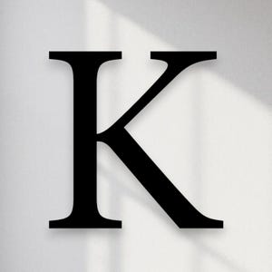 May include: A large, black letter "K" against a white background. The letter is in a serif font, with a classic, elegant design. The image has a minimalist aesthetic, with soft shadows adding depth.