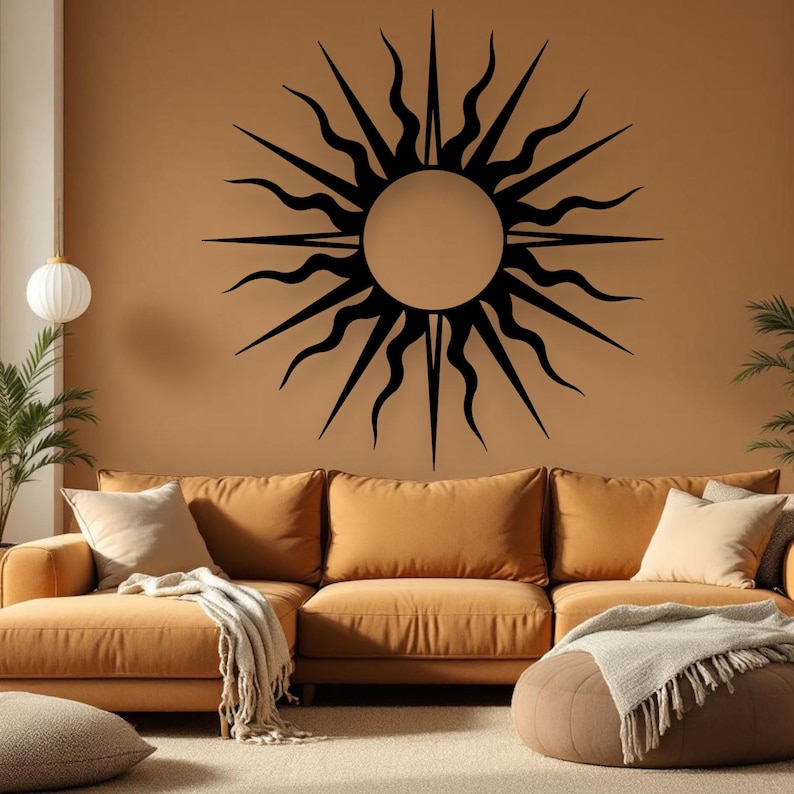 May include: A large, black sunburst wall art decorates a tan wall above a mustard-coloured sectional sofa. The sun design features a central circle with radiating, stylized flames. The room is decorated with neutral-toned pillows and a blanket.