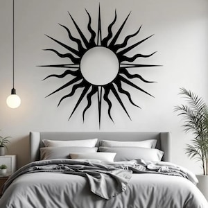 May include: A black metal sunburst wall decoration featuring a circular centre and radiating pointed and wavy rays. The sunburst is mounted on a white wall above a bed with grey bedding. A modern bedroom decor.