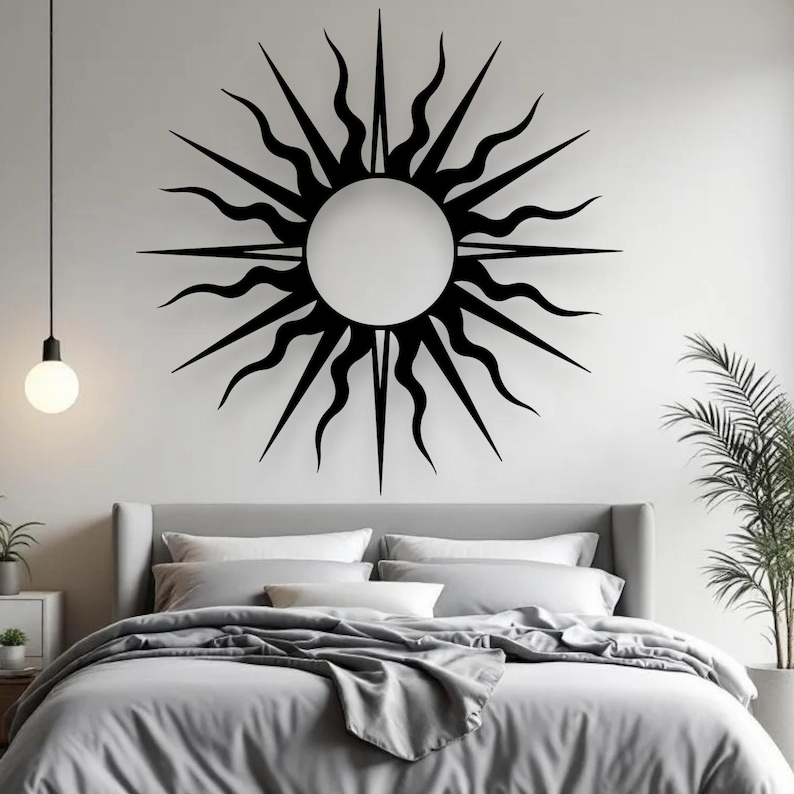 May include: A black metal sunburst wall decoration featuring a circular centre and radiating pointed and wavy rays. The sunburst is mounted on a white wall above a bed with grey bedding. A modern bedroom decor.