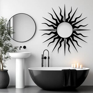 May include: A contemporary bathroom featuring a black oval bathtub, a circular mirror, and a black sunburst wall decoration. A white pedestal sink and a potted plant enhance the minimalist style. The room is painted white, creating a clean and stylish aesthetic.