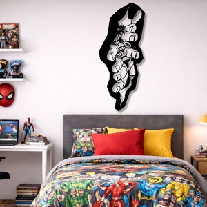 May include: A black and white metal wall art piece showing a comic book character's hand reaching out. The artwork is mounted on a white wall above a bed with a comic book-themed duvet cover and pillows. The room is decorated with superhero-themed items.