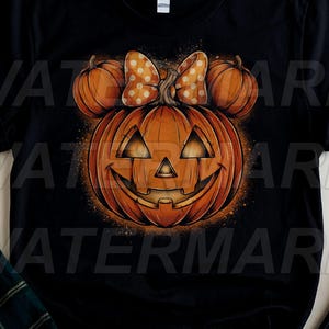 May include: A black short-sleeved t-shirt featuring a central graphic of a large orange jack-o'-lantern with two smaller pumpkins positioned above it to resemble ears. A polka-dot bow sits between the smaller pumpkins on the main pumpkin.