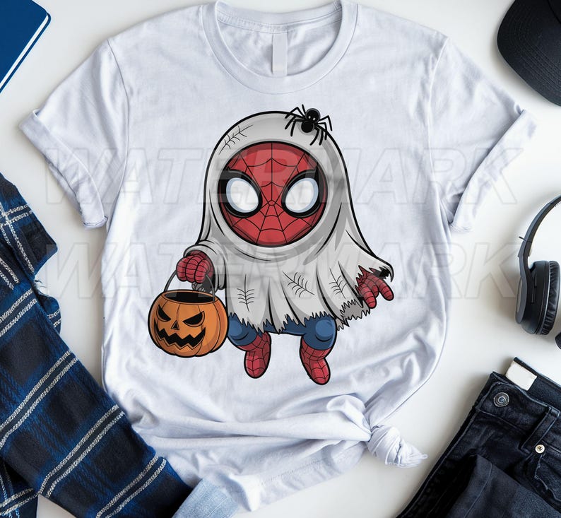 Op de afbeelding: Een wit t-shirt met korte mouwen en een afbeelding van een personage in een wit spookkostuum met een rood en zwart webmasker. Het personage houdt een oranje pompoen-snoepemmer vast en heeft een kleine zwarte spin op het hoofd.