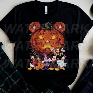 May include: A black short-sleeve t-shirt featuring a large orange jack-o'-lantern with Mickey Mouse-shaped ears and a group of cartoon characters dressed in Halloween costumes, including a witch, a vampire, a mummy, and a ghost.