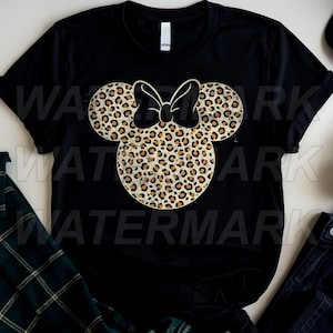 May include: A black short-sleeved t-shirt featuring a large, centered graphic of a mouse-ear silhouette with a bow, filled with a tan and brown leopard print pattern. The design has a distressed, weathered texture throughout the print.