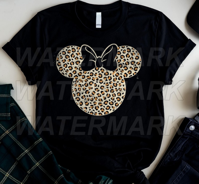 May include: A black short-sleeved t-shirt featuring a large, centered graphic of a mouse-ear silhouette with a bow, filled with a tan and brown leopard print pattern. The design has a distressed, weathered texture throughout the print.