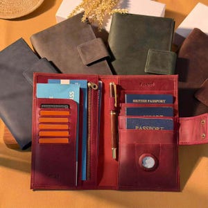 May include: A burgundy leather travel wallet featuring multiple card slots, a zippered pocket, a pen loop with a brown pen, and several interior sleeves holding passports. The wallet includes an embossed RFID label and a circular cutout.