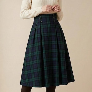 Puede incluir: Un suéter color crema combinado con una falda plisada hasta la rodilla con un estampado de cuadros verdes y azul marino. La falda tiene una cintura alta con botones decorativos. Botines negros completan el conjunto, adecuado para otoño o invierno.