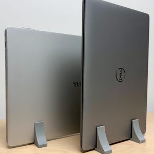May include: Two laptops on gray laptop stands. The laptop on the left is silver and the laptop on the right is gray with a Dell logo.