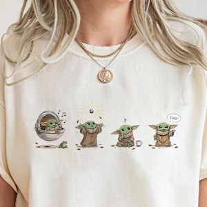 May include: Cream-colored t-shirt featuring a graphic of a character from a popular science fiction series. The graphic shows the character in four different poses. The word "Cool" is written in a speech bubble.