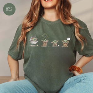 May include: Moss green t-shirt featuring a series of Grogu illustrations. The illustrations depict Grogu in various poses, including one with a bubble that says "Cool!". The shirt is a relaxed fit.