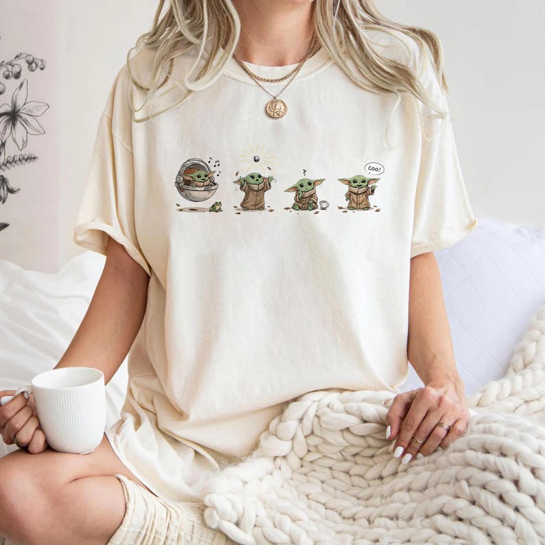 May include: Cream-colored t-shirt featuring a graphic of a character from a popular science fiction series. The graphic shows the character in four different poses. The word "Cool" is written in a speech bubble.