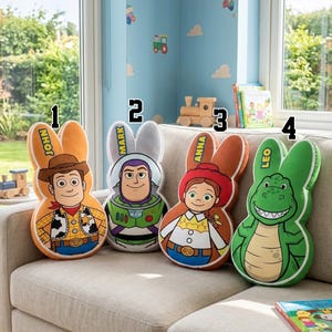 May include: Four character-shaped pillows with bunny ears are displayed on a beige couch. The pillows feature Woody, Buzz Lightyear, Jessie, and Rex from Toy Story. Each pillow has a name printed on the ear: John, Mark, Anna, and Leo.