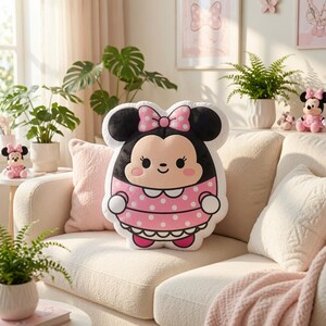 May include: A plush pillow shaped like a cartoon character with black ears, a pink polka-dot bow, and a matching pink polka-dot dress. The character has a light tan face, black eyes, and a small smile, featuring a white collar and white cuffs.