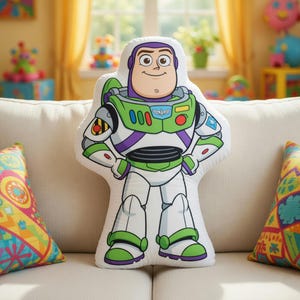 以下が含まれることがあります： 緑、紫、白のディテールが施された、白いバズ・ライトイヤーの形をしたクッション。クッションには、バズ・ライトイヤーの顔と宇宙服のデザインが施されています。クッションは、カラフルなクッションが置かれた白いソファの上にあります。