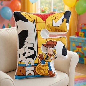 Peut inclure: Un coussin d&eacute;coratif avec un design inspir&eacute; du personnage Woody de Toy Story. Le coussin a la forme de la lettre "F" et pr&eacute;sente un sch&eacute;ma de couleurs jaune, rouge et blanc avec le nom "JACK" imprim&eacute; dessus.