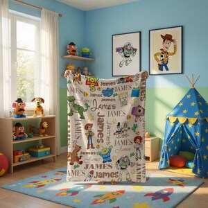 Puede incluir: Una manta de forro polar blanca con un patr&oacute;n repetitivo de personajes de Toy Story, incluyendo a Woody, Buzz Lightyear, Rex y Slinky Dog, intercalados con el nombre James en varias fuentes y el logotipo de Toy Story 5 en rojo, amarillo y azul.