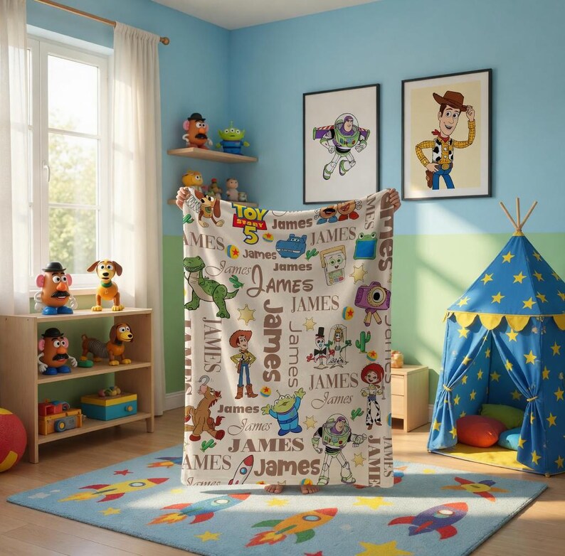 Puede incluir: Una manta de forro polar blanca con un patr&oacute;n repetitivo de personajes de Toy Story, incluyendo a Woody, Buzz Lightyear, Rex y Slinky Dog, intercalados con el nombre James en varias fuentes y el logotipo de Toy Story 5 en rojo, amarillo y azul.