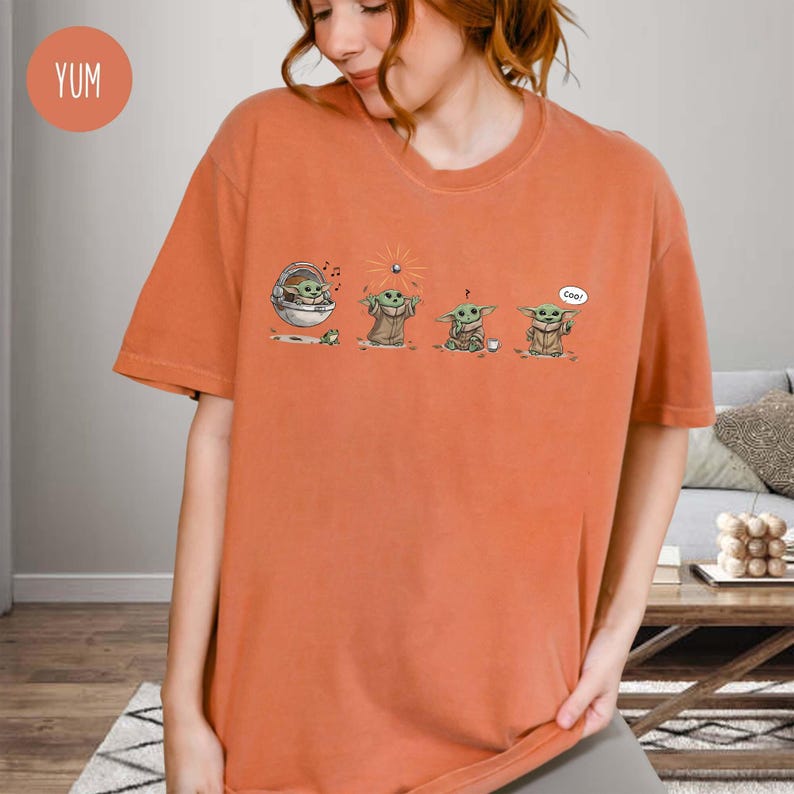 May include: Orange t-shirt featuring a graphic of a character from a popular science fiction series. The graphic shows the character in four different poses. The word "cool" is in a speech bubble. The shirt is a solid orange color.