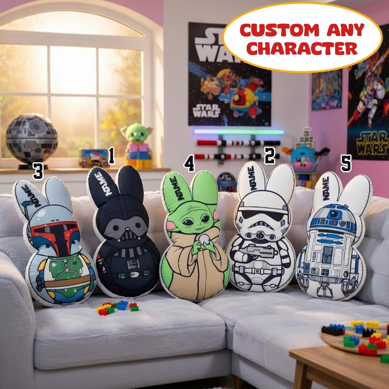May include: Five Star Wars character-themed bunny cushions are displayed on a gray sofa. The cushions feature characters like Darth Vader, a Stormtrooper, and Baby Yoda. The cushions have the word "NAME" on the ears. The image also includes a Death Star model and Star Wars posters.
