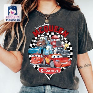 May include: Dark grey t-shirt with a colourful graphic of characters from the animated film Cars. The design includes Lightning McQueen and other vehicles, with the text "Lightning McQueen" and "Cars".
