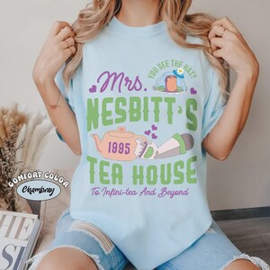 May include: Light blue t-shirt with the text "Mrs. Nesbitt's Tea House" and a teapot graphic. The shirt also features the text "You see the hat?" and "To Infini-tea And Beyond". The shirt is made of Comfort Color Chambray material.