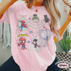 May include: Pink t-shirt featuring a Spidey and Amazing Friends graphic. The design includes cartoon images of Spider-Man, Hulk, Black Panther, and Spider-Gwen, along with the text "Spidey Amazing Friends". The shirt is a Comfort Color Blossom.