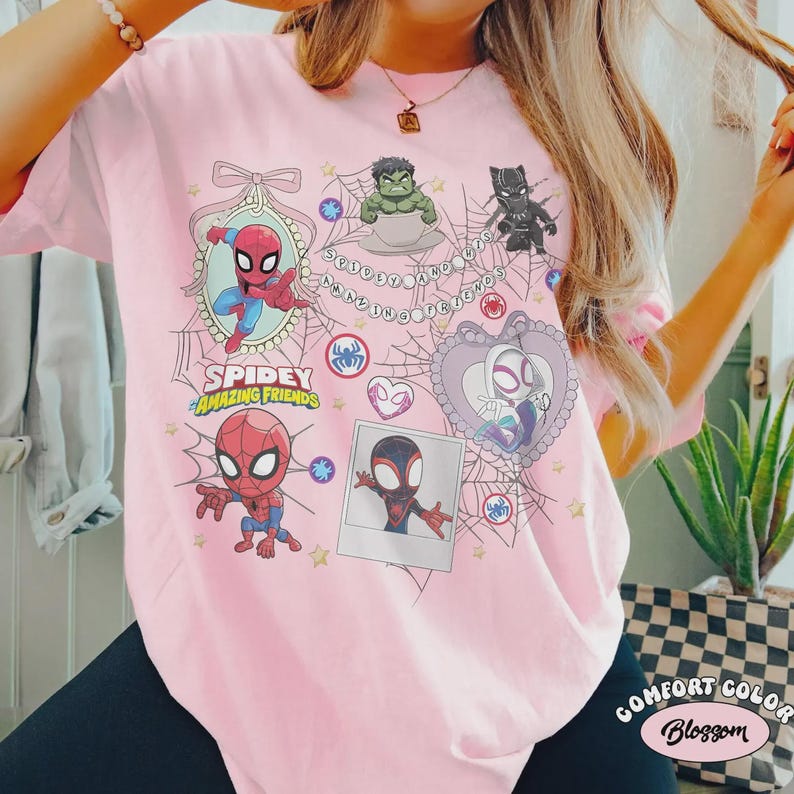 May include: Pink t-shirt featuring a Spidey and Amazing Friends graphic. The design includes cartoon images of Spider-Man, Hulk, Black Panther, and Spider-Gwen, along with the text "Spidey Amazing Friends". The shirt is a Comfort Color Blossom.