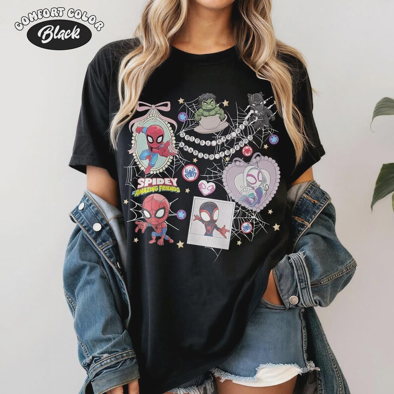 May include: Black Comfort Colors t-shirt featuring a colorful graphic of Spider-Man and friends. The design includes various characters, hearts, and the text "Spidey and His Amazing Friends". The shirt has a crew neck and short sleeves.