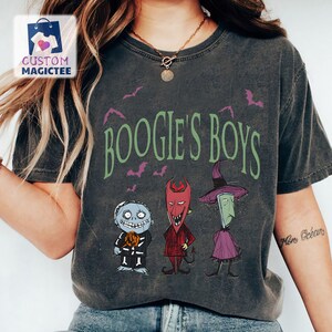 May include: Dark gray t-shirt featuring the phrase "Boogie's Boys" in green, with purple bats. The shirt displays three cartoon characters in Halloween costumes. The shirt has a vintage, worn look.