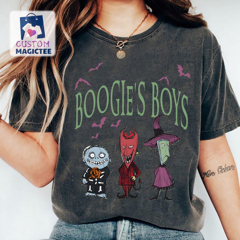 May include: Dark gray t-shirt featuring the phrase "Boogie's Boys" in green, with purple bats. The shirt displays three cartoon characters in Halloween costumes. The shirt has a vintage, worn look.