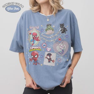 May include: Blue jean Comfort Colors t-shirt featuring cartoon illustrations of Spider-Man, Hulk, Black Panther, and Spider-Gwen. The shirt has the words "Spidey Amazing Friends" and a spider web design.