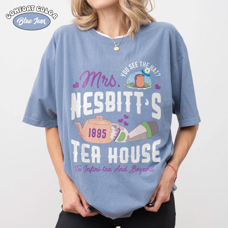 May include: Blue jean Comfort Colors t-shirt with a graphic design. The design includes the text "Mrs. Nesbitt's Tea House" with a teapot, the year 1995, and the phrase "To Infini-tea And Beyond".