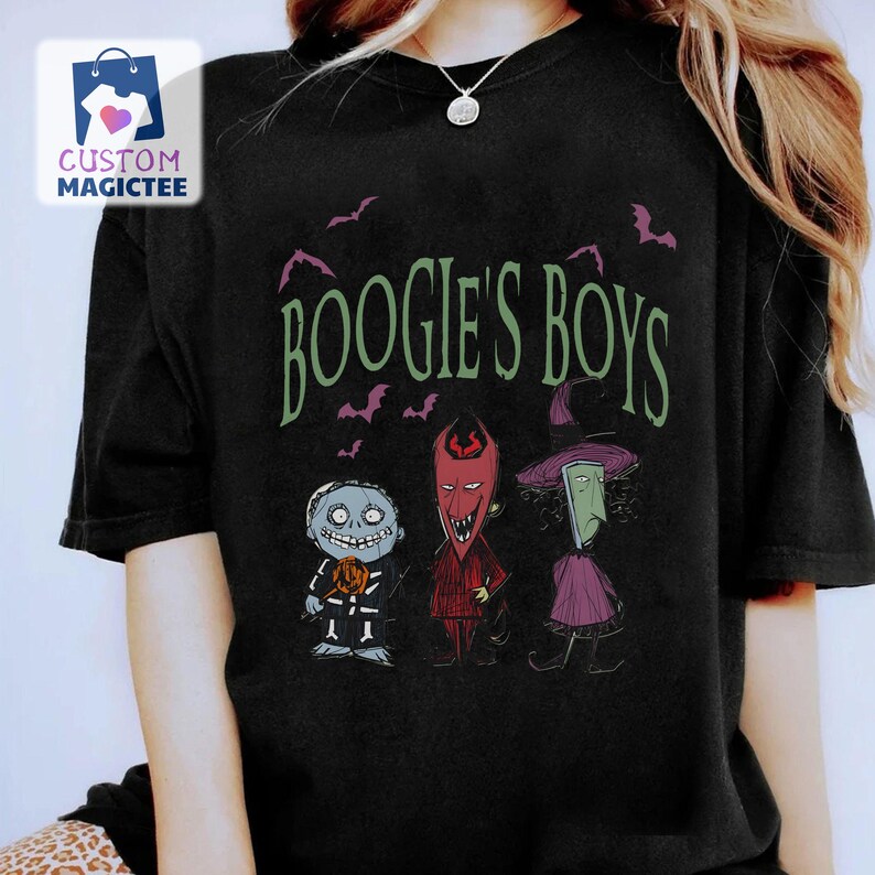 May include: Black t-shirt featuring the phrase "Boogie's Boys" in green, with illustrations of three characters. The characters include a skeletal figure, a devil-like figure, and a witch-like figure. Purple bats are scattered around the text.