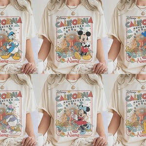 Könnte beinhalten: Cremefarbene T-Shirts mit Disney-Figuren und dem Text "Disney California Adventure". Jedes Shirt zeigt eine andere Figur: Donald Duck, Mickey Mouse, Goofy, Daisy Duck, Minnie Mouse und Pluto. Die Shirts haben ein Vintage-Retro-Design.