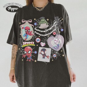 May include: Dark gray t-shirt featuring cartoon images of Spider-Man and other characters. The shirt has the words "Spidey and His Amazing Friends" printed on it, along with the Comfort Color and Pepper logos.