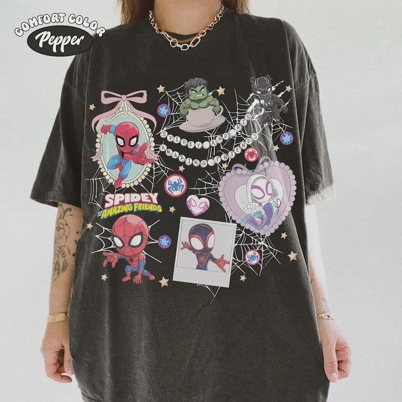 May include: Dark gray t-shirt featuring cartoon images of Spider-Man and other characters. The shirt has the words "Spidey and His Amazing Friends" printed on it, along with the Comfort Color and Pepper logos.