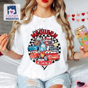 May include: White t-shirt with a colourful graphic of characters from the Cars film, including Lightning McQueen. The design features the text "Lightning McQueen" and "Cars" in red and black, set against a chequered background.