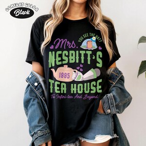 May include: Black Comfort Colors t-shirt with a graphic that reads "Mrs. Nesbitt's Tea House" in green and purple. The design includes a teapot, a teacup, and the text "To Infini-tea And Beyond."